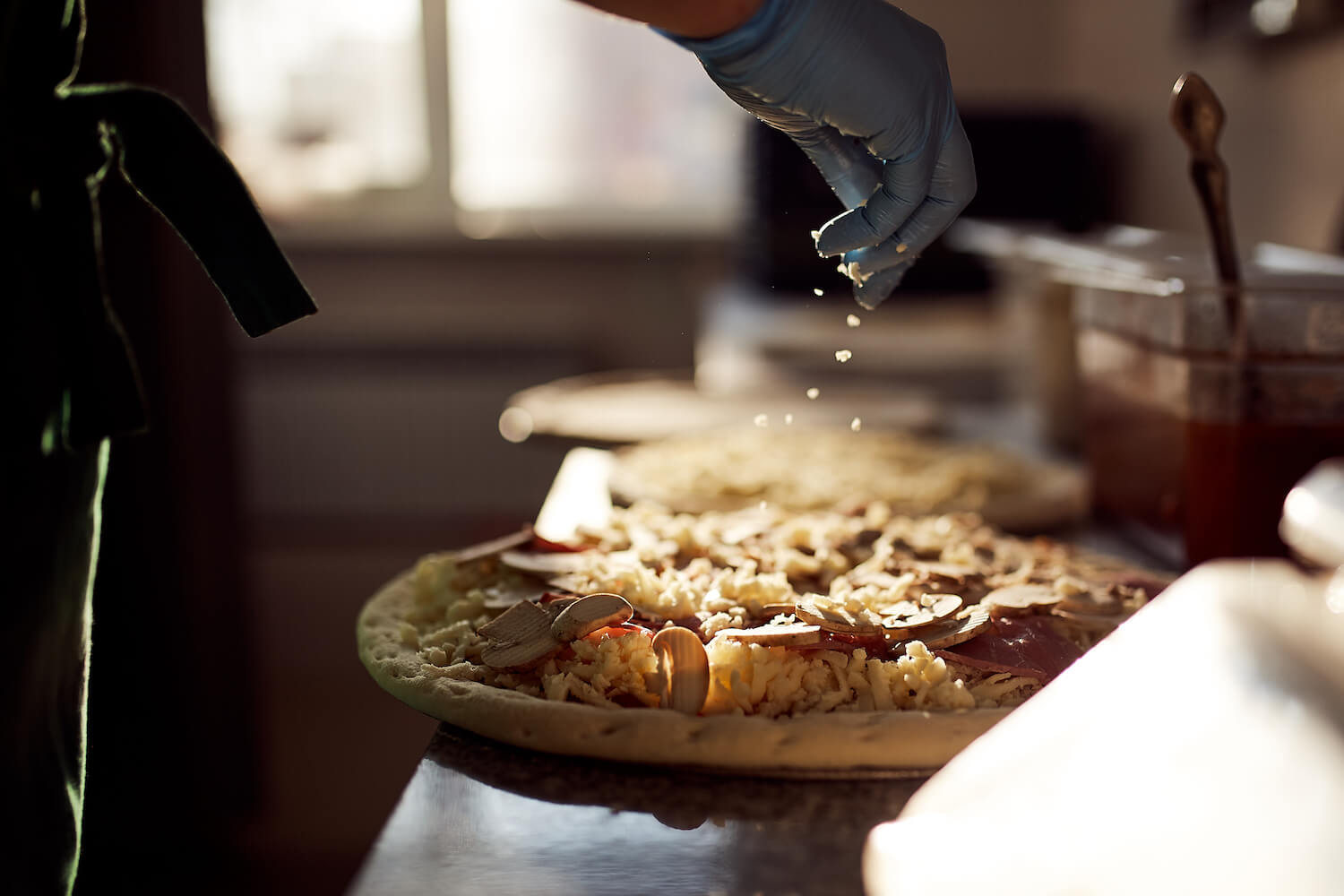 Сотрудница пиццерии «О-пицца» посыпает пиццу сыром моцарелла
